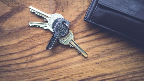 Nycklar för låstjänster liggandes på brunt bord med läder-plånbok bredvid